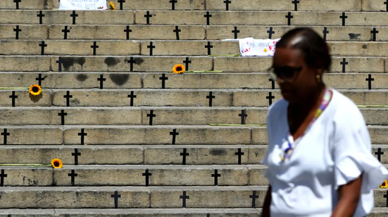 Mulher caminhando em frente a um mural em homenagem às vítimas. - Tânia Rêgo/Agência Brasil